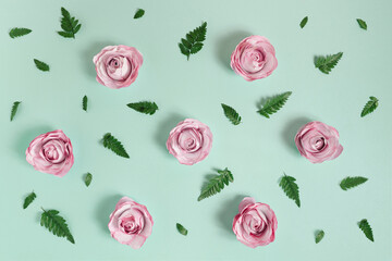 Creative pattern made of pink paper roses and real leaves on bright green background. Minimal...