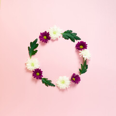 Spring round wreath made of flowers and leaves on pastel pink background. Natural round frame layout with copy space. Flat lay visual.