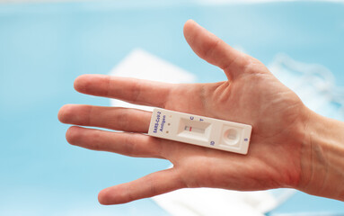 On palm of woman lies antigen test on coronavirus. Make fast test at home and get results. On pale blue blurred background lies medical masks. Close-up