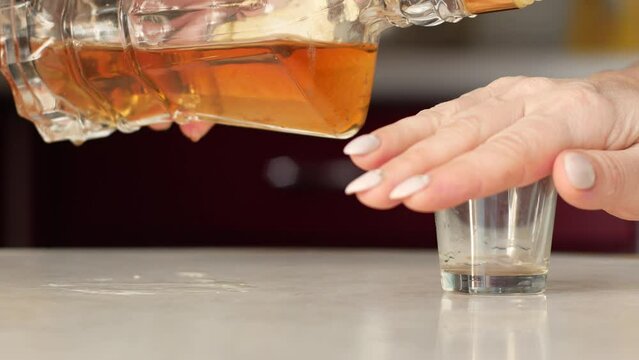 Close-up of a woman's hand forbids pouring alcohol into a glass of whiskey. A woman denies taking strong alcohol closes her glass with her palm. Treatment of alcoholism in women. selective focus
