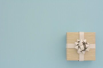 
One BEIGE gift box with silver ribbon and bow on light blue table background. Minimal festive gift...