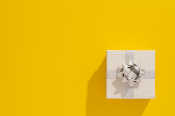 
One grey gift box with silver ribbon and bow on yellow table background. Minimal festive gift...