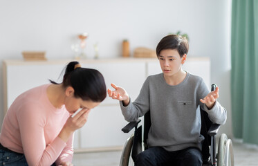 Unhappy mother crying and her disabled teen son in wheelchair trying to justify himself after...