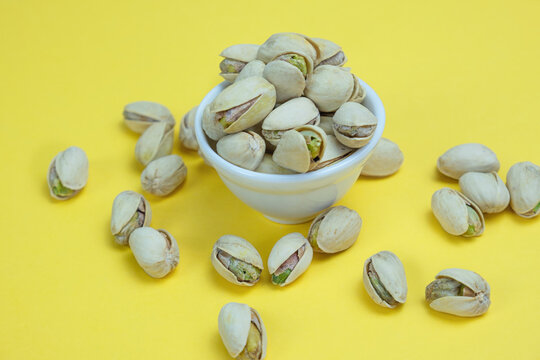 Roasted salted pistachios in a white ceramic bowl on a yellow background