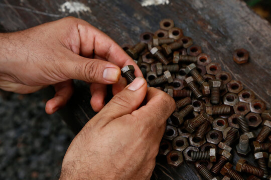 Hands of a mechanic or worker. Man working with rusty nuts and bolts. Manual work table. Oil dirty hands. Employee. Worker. Close up. Nut and bolt insert.