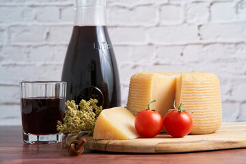 Italian hard cheese such as pecorino or caprino, wine with carafe and traditional glass, tomato and oregano. Sliced dried cheese with a bunch of oregano on a wooden board.  - obrazy, fototapety, plakaty