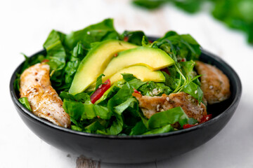 Healthy  vegetable buddha bowl salad with fried chicken and avocado, peppers and leaf lettuce on a white plate.
