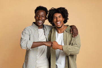 Portrait Of Two Cheerful Black Guys Embracing And Making Fist Bump Gesture