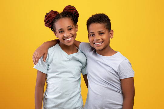Loving black brother and sister hugging on yellow background