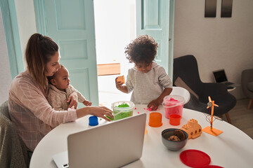 Little boy playing with kinetic sand at home near his mother and brother
