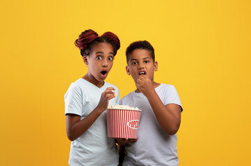 Emotional black kids boy and girl eating popcorn, watching movie