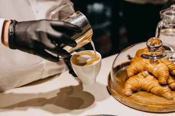 Barman drawing a heart on cappuccino foam, in a white cup.
