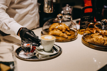 Barman serving a cappuccino with a heart shaped picture on foam, in a white cup on a bar counter.