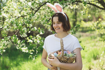Easter egg hunt in spring garden. Funny teen girl with eggs basket and bunny ears on Easter egg...