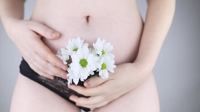 Close-up of a woman body. Female pubis. Panties from which flowers stick out. Concept photo about feminine intimate health. Delicate and sensual frame without a hint of eroticism. Selective focus.