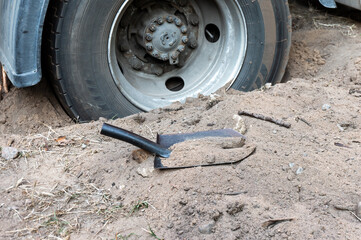 Truck  wheel is stuck in the sand. Shovel nearby.