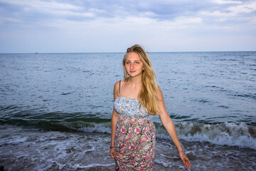 a young girl in the evening on the seashore in a sundress and with a hat   