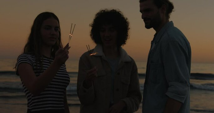 Friends enjoying sparklers while playing on beach during sunset