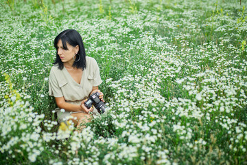 Female photographer sitting outdoors on flower field landscape holding a camera,