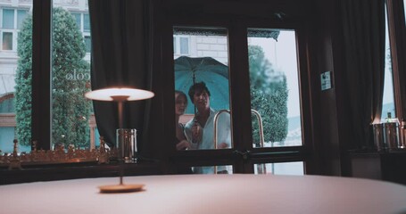 Couple holding umbrella contemplate entering restaurant 