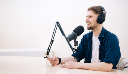 Man recording podcast in white studio. hand holding mobile phone in audio home studio. Male with...