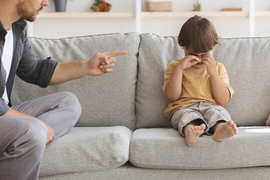 Child abuse concept. Unhappy little boy sitting on sofa and crying, unrecognizable angry father scolding at upset kid - Powered by Adobe