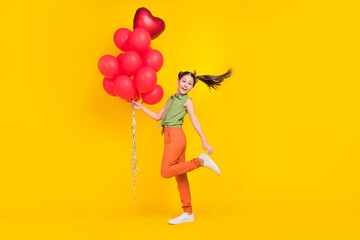 Photo of funky cute preteen girl dressed green top holding red bubbles walking smiling isolated yellow color background