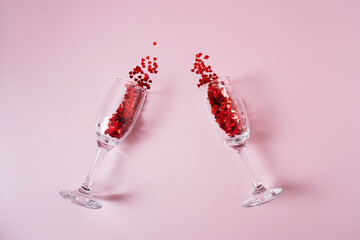 Heart made of pink and red beads pouring out from two transparent wine glasses on the pink background.