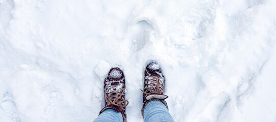 banner with Legs in burgundy boots and blue jeans in the snow. Footprints in the snow. Winter...