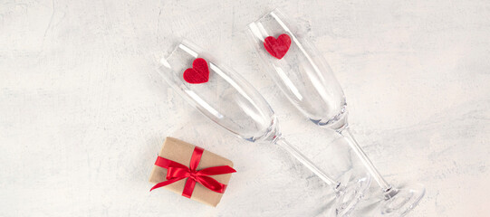Fototapeta na wymiar Two glasses, a gift and red hearts on white stone background. Valentines day background. Valentine's day concept. Flat lay. View from above.