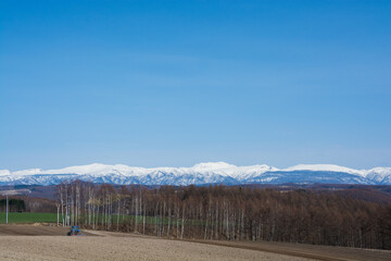 春の晴れた日の農作業と雪山　十勝岳連峰
