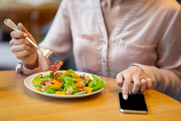 Calories counting and food control concept. Woman using smartphone with black screen and eating fresh salad