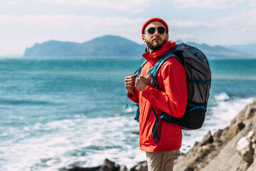 A bearded traveler with a backpack on the background of the sea. Portrait of a traveler in red...
