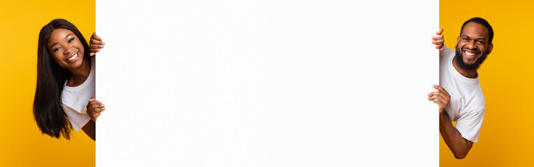 African couple peeking out blank white advertising billboard at studio