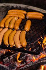 Sausages grill on the black grate above the fire.