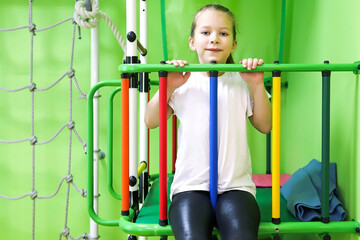 The girl smiles, plays and goes in for sports on the stairs and the Swedish wall in the children's center in special tight clothes and leads a healthy lifestyle under the supervision of her parents