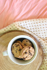 Mug filled with chocolate chip cookies and soft knitted blanket on a bed. Flat lay.