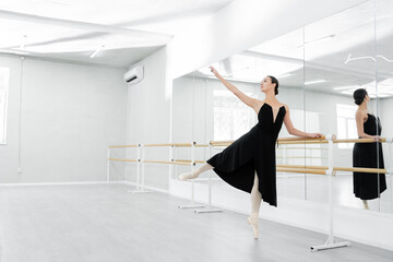 Fototapeta na wymiar graceful woman in black dress rehearsing near mirrors in ballet studio