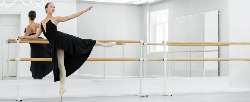slim and graceful ballerina practicing ballet elements at barre in studio, banner