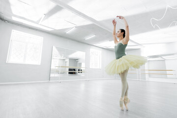 full length view of ballerina in tutu dancing with raised hands in spacious studio