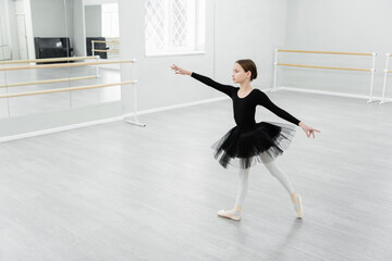 full length view of girl in black tutu dancing during repetition in studio