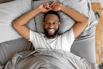 Young African American man lying in bed after waking up