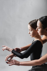 side view of dance teacher showing ballet elements to girl on grey background