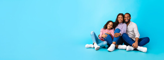 Black husband hugging smiling lady and girl, sitting on floor