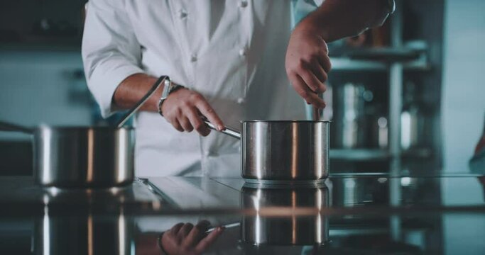 Chef calmly stirs pot while chef 2 moves in background