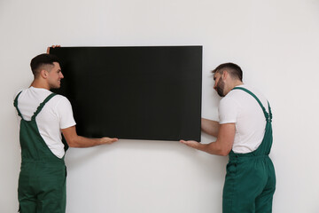 Professional technicians installing modern flat screen TV on wall indoors