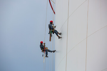 Male workers control rope down height tank rope access inspection of thickness shell plate tank.