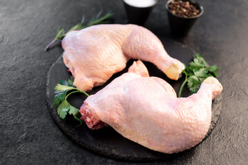 two raw chicken legs with spices and herbs on a stone background