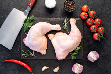 two raw chicken legs with spices and herbs on a stone background