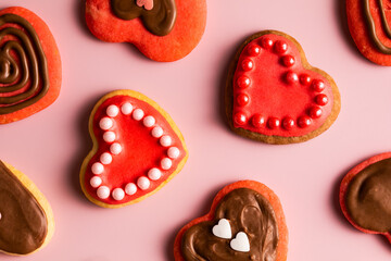 Top view of cookies in shape of hearts decorated by pink icing, chocolate and sprinkles on solid pale pink background
